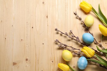 Easter eggs, beautiful tulips and willow branches on wooden background, flat lay. Space for text