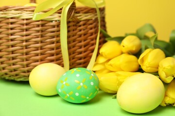 Easter eggs and beautiful tulips on green table, closeup