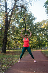 A mature, fit woman and man doing jumping jacks in a city park during summer, enjoying an active...