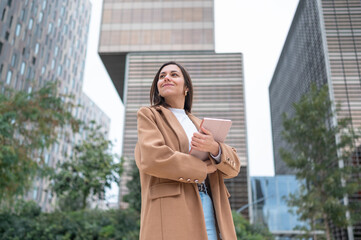 Businesswoman holding tablet and looking up at modern buildings in the city