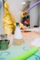 The animator conducts an experiment, a chemical experiment with liquid nitrogen in a flask with a white cloud on the table, showing a super show at a children's party.