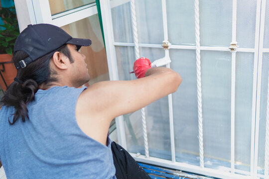 Latino worker of Mexican origin carrying out his work, painting a fence with white paint, happy, relaxed and dirty
