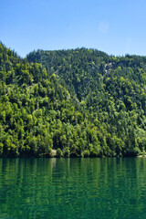 Green trees on a hill over rippling green water at Konigssee in Bavaria, Germany on a sunny spring day.