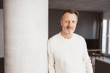 Confident senior man in white sweater leaning against concrete column