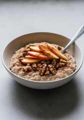 Bowl of oatmeal with apple slices, walnuts, and cinnamon on gray surface
