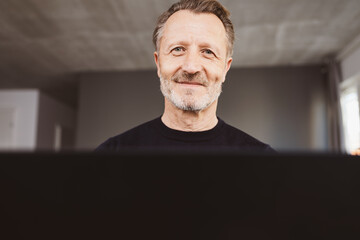 Smiling senior man in black sweater looking at laptop