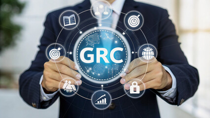 Obraz premium Businessman holding a tablet displaying a GRC system interface.