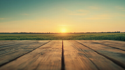 Fototapeta premium Featuring an empty wooden table set against a vast green field, basking in the warm glow of a golden sunset on the horizon