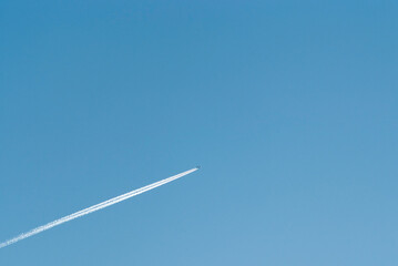 airplane in flight and white stripe against blue sky