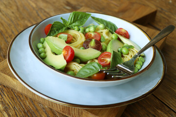 Pasta salad with green peas, avocado, cherry tomatoes and basil on rustic wooden background. Top view.