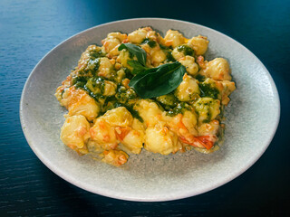 Gnocchi con ricotta e pesto Genovese, ricotta lemon sauce with thin ruffled carrots, Cherry tomatoes and basil on dark emerald green background, traditional Italian cuisine, high angle view