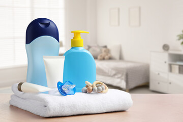 Set of baby cosmetic products, towel, pacifier and teether on table in room. Space for text