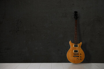 Naklejka premium Modern electric guitar on floor near black grunge wall. Space for text