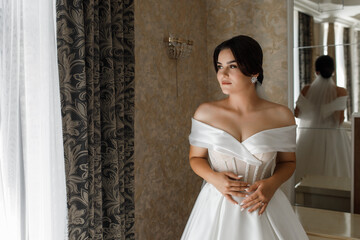 bride woman in wedding dress. The dress is white with open shoulders and a corset, which is...