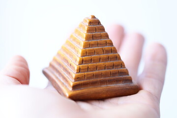 A person holds a small wooden pyramid in their hand, perfect for use in images about spirituality, mysticism or symbolism.