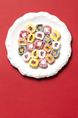 Assorted Turkish delight on a white plate. Colorful sweets with powdered sugar. Placed on a red background. Traditional festive treat for Nowruz.