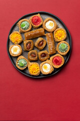 Assorted baklava and Middle Eastern sweets on a black plate. Colorful pastries with nuts and syrup. Placed on a red background. Traditional festive dessert for Nowruz.