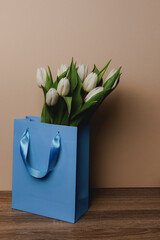 A bouquet of beautiful white tulips in a blue paper bag without inscriptionson a light background.  Minimalistic modern background with copy-space.

International Women's day, mother's day greeting c
