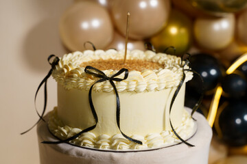 Elegant cake decoration featuring black ribbons on a festive backdrop with balloons for a special celebration