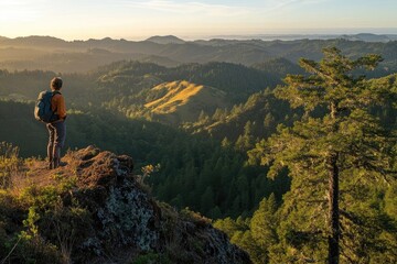 A lone hiker pauses atop a mountain, taking in the breathtaking panorama of sunlit hills and valleys.