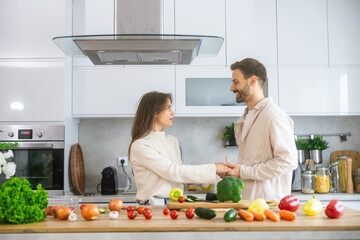 A joyful couple enjoys cooking together, holding hands in a bright kitchen filled with fresh vegetables and a warm atmosphere.