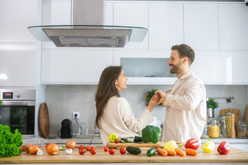 A happy couple shares laughter and dance in their kitchen, preparing fresh vegetables together filled with love.