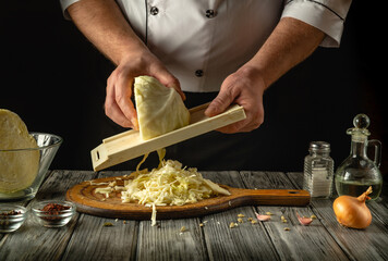 In a cozy kitchen, a chef expertly shreds fresh cabbage using a mandoline. Surrounding ingredients include onions, garlic, and spices, hinting at a flavorful recipe in progress