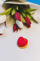 A decorative heart-shaped piece rests on a smooth surface near a bouquet of vibrant red and white tulips, capturing a moment of love and affection. The setting feels warm and inviting