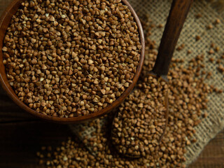 Organic buckwheat groats in a wooden bowl with a spoon on a linen napkin on a wooden table.