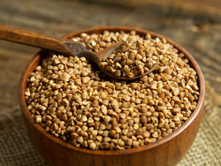 Organic buckwheat groats in a wooden bowl with a spoon on a linen napkin on a wooden table.