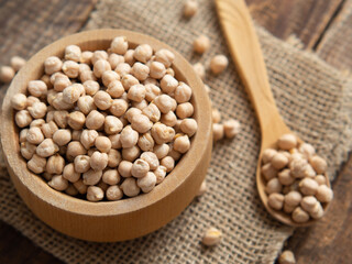 Close-up of a bowl filled with raw chickpeas surrounded by scattered legumes and a wooden spoon