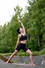 Woman in reverse warrior pose, arching side body and reaching upward in serene forest setting