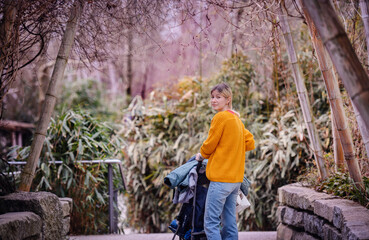Obraz premium Young mother in a vibrant yellow sweater pushing a stroller along a serene park pathway