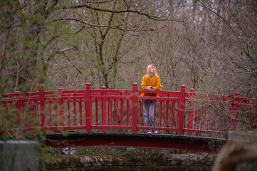 A thoughtful young woman stands on a vibrant red bridge, surrounded by the tranquility of autumn...