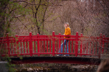 A thoughtful young woman stands on a vibrant red bridge, surrounded by the tranquility of autumn...