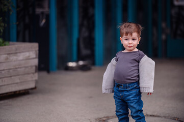 A young boy stands confidently on a city street, casually draped in a sweater over his shoulders