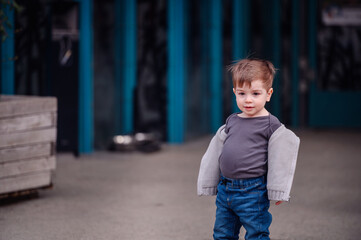 A young boy stands confidently on a city street, casually draped in a sweater over his shoulders