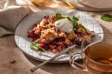 Apple crumble with ice cream on top decorated with mint leaves served in a plate on beige...