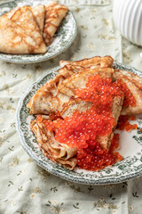 Pancakes or crepes with red caviar on a plate on linen tablecloth background close up. Blini for Maslenitsa, recipe Pancake day