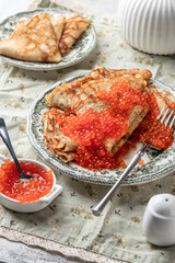 Pancakes or crepes with red caviar on a plate on linen tablecloth background. Blini for Maslenitsa, recipe Pancake day