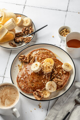 Healthy oatmeal pancakes with banana, nuts and honey on white tile background and coffee. Morning breakfast concept. Pancake day or Maslenitsa recipe