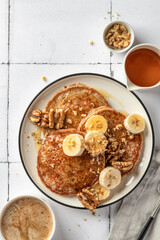 Healthy oatmeal pancakes with banana, nuts and honey on white tile background. Morning breakfast, top view. Pancake day or Maslenitsa recipe