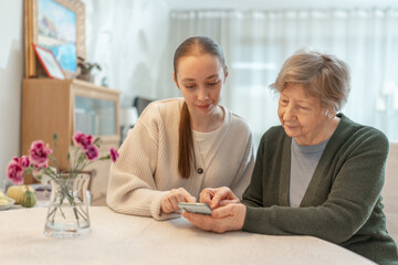 Young woman helping an senior woman with a smartphone at home. Concept of technology, education,...