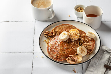 Healthy oatmeal pancakes with banana, nuts and honey on white tile background. Morning breakfast. Pancake day or Maslenitsa recipe, copy space