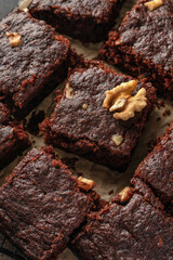 Chocolate brownie cake dessert with nuts on baking rack on dark background close up, texture