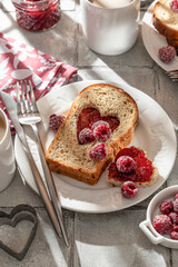 Toasted bread with heart-shaped cut and raspberry jam on tile background in bright morning light. Festive breakfast for Valentines day