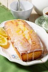 Aromatic lemon cake, covered with sugar icing and sprinkled with zest, served with tea.