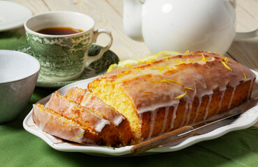 Aromatic lemon cake, covered with sugar icing and sprinkled with zest, served with tea.