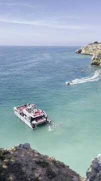 Vista deslumbrante das fal&eacute;sias do Algarve, com &aacute;guas cristalinas e a tranquilidade do ver&atilde;o. Um barco e caiaques passam suavemente pelas &aacute;guas turquesa, criando uma cena perfeita de um dia relaxante 