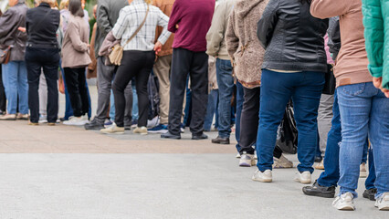 Group of anonymous diverse people standing in queue outdoors, long line of men and women, rear...
